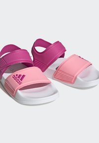Ružové a fialové sandále s gumovými popruhmi, textúrovanou stielkou a bielou podrážkou. Na ružovom popruhu je umiestnené logo adidas.