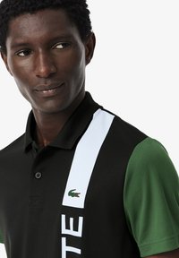 Polo nero e verde con una striscia bianca e dettagli del logo, realizzato in tessuto testurizzato con colletto e dettagli dei bottoni.