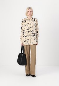 Beige button-up shirt with black and grey abstract patterns, paired with light brown trousers and a black tote bag.