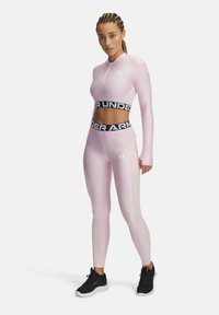 Completo sportivo rosa chiaro con crop top a maniche lunghe e leggings a vita alta, caratterizzato da una fascia in vita nera con logo e una texture liscia.