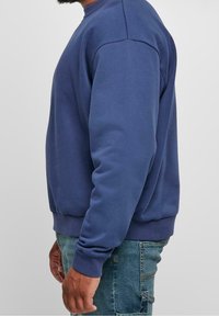 Sudadera azul con un clásico cuello redondo, puños y dobladillo de canalé. La tela parece suave con una textura lisa, diseñada para la comodidad.