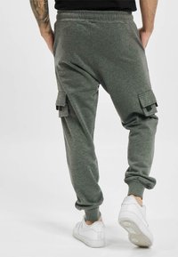 Graue Cargo-Sweatpants mit elastischem Bund, schmal zulaufenden Beinabschlüssen und seitlichen Taschen, aus einem weichen Material. Getragen mit weißen Sneakers.