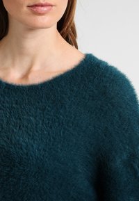 Teal fluffig stickad tröja med vid halsringning, som har en mjuk textur och lös passform, vilket ger en lyxig, plyschig look.