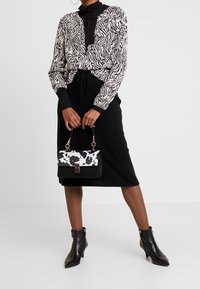 Blusa a righe zebrate in bianco e nero con maniche lunghe, abbinata a una gonna nera. Una borsa a tracolla con motivo in bianco e nero completa l'outfit.