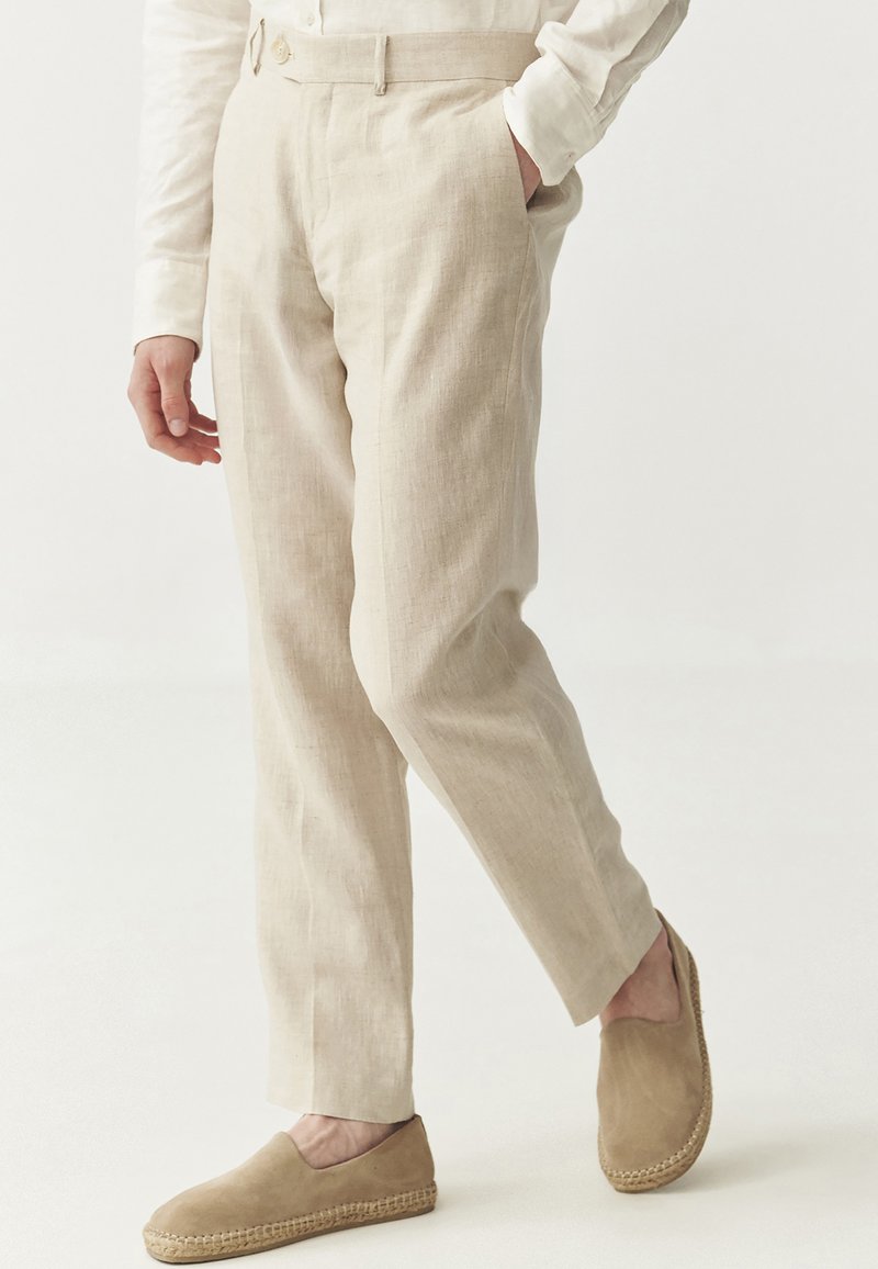 Beige Leinenhosen mit geradem Schnitt, Fronttaschen und Knopfverschluss, kombiniert mit hellbraunen Espadrilles.