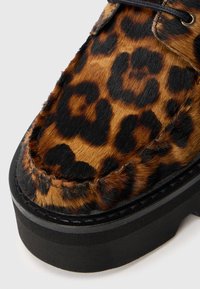 Pladevibrator sko med leopardprint og en pelslignende tekstur, sorte syninger og en tyk sort gummisål. Har rund tå og snørebåndsdesign.