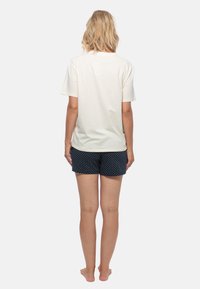 Weißes Baumwoll-T-Shirt kombiniert mit navyblauen Shorts mit Punkten, beide im lässigen Schnitt. Die Shorts haben einen elastischen Bund. Schlichte Rückansicht.