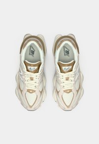 Pantofi sport cu partea superioară din plasă alb-crem, accente din piele intoarsă bej și șireturi de culoare deschisă. Designul include o talpă groasă și detalii cu logo.