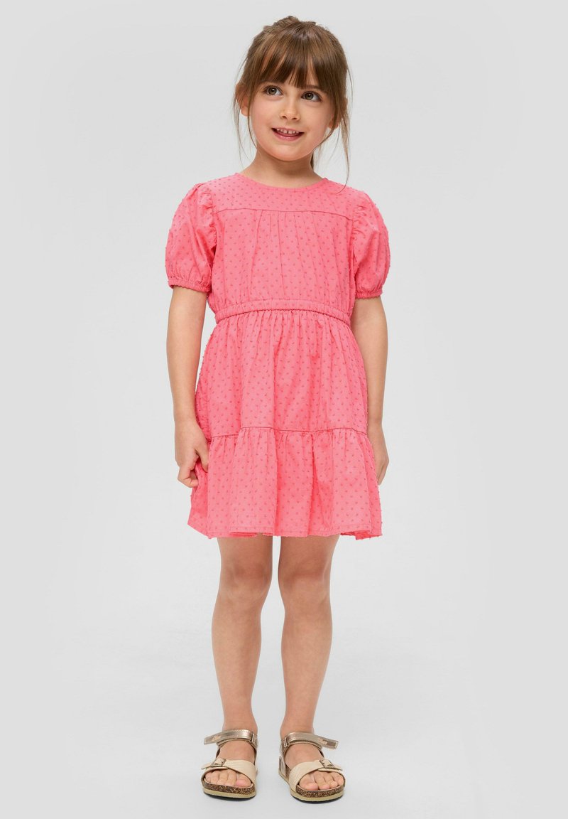 Rosa kurzärmliges Kleid mit strukturierten Punkten, gerafftem Taillenbereich und gestuftem Rock. Getragen mit hellbraunen Sandalen mit einer Schleifen-Detail.