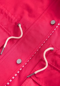 Tela de color rosa brillante con cordones blancos pasados por ojales metálicos y botones redondos plateados a lo largo de los bordes cosidos.