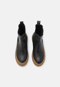 Bottines en cuir noir avec un bout arrondi, des panneaux latéraux élastiques et une semelle en caoutchouc marron clair. Caractéristiques : une languette à l'arrière.