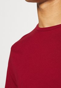 Röd bomullströja med rund halsringning och korta ärmar, med en mjuk textur och en enkel design.