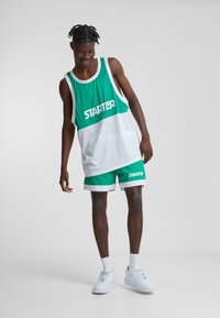 Grøn og hvid atletisk tanktop med "STARTER" logo, parret med matchende shorts. Har åndbart stof og sporty design. Hvide sneakers.