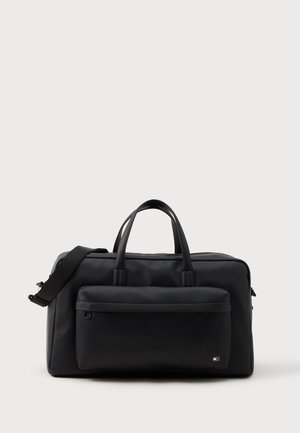 Sac de voyage rectangulaire noir avec deux poignées, une bandoulière et une grande poche frontale zippée sur un fond clair uni.