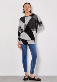 Zwarte en grijze geometrisch patroon oversized trui gecombineerd met blauwe skinny jeans en zwarte ballerina's. Glad textuur, ontspannen pasvorm, brede mouwen.