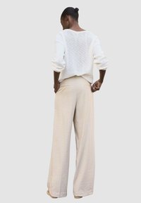 Pull en tricot texturé léger, blanc, à coupe ample et manches larges, associé à un pantalon large beige taille haute.