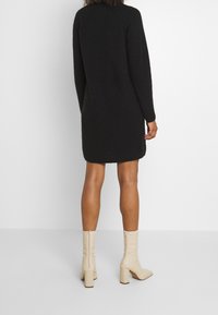 Robe tricotée noire avec des manches longues et un ourlet arrondi, associée à des bottines beiges à fermeture éclair avec un talon carré.