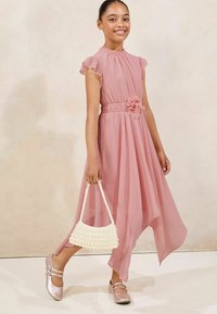 Roza chiffon haljina s volanima, suženim strukom i detaljem cvijeta. Uparen s bijelom torbicom od perlica i sjajnim ružičastim cipelama.