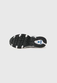 Suela de zapatilla de goma negra con una superficie texturizada, acentos blancos y detalles azules en la zona del talón. Diseñada para tracción y soporte.