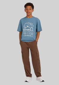 Blue cotton t-shirt with white graphic design, paired with brown cargo pants featuring side pockets, and white athletic shoes.