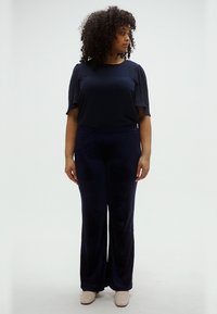 Μπλε ναυτικό τοπ με κοντά, υφασμένα μανίκια, συνδυασμένο με παντελόνι σε φαρδυά γραμμή στο ίδιο χρώμα και μπεζ παπούτσια. Ομαλό ύφασμα και απλός, κομψός σχεδιασμός.