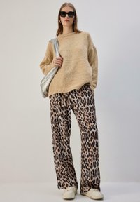 Beež värvusega kampsun lõdva lõikega, mida on kombineeritud laiade lõhikutega leopardimustriliste pükstega ja valgete spordijalatsitega. Hõbedane õlakott lisab aksenti.