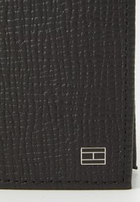 Black textured leather wallet featuring a patterned surface and a metallic logo accent. Edge stitching is visible along the seams.
