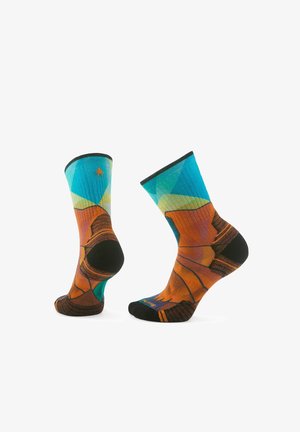 Mehrfarbige Crew-Socken mit geometrischen Mustern, die Blau-, Orange- und Grüntönen, sowie schwarzen Akzenten an Ferse und Zehen aufweisen.