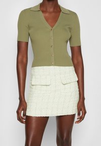 Oliwkowa, prążkowana bluzka z dekoltem w kształcie litery V, krótkimi rękawami i złotymi guzikami, w połączeniu z jasnoskalnym, teksturowanym mini spódnicą z dwiema przednimi kieszeniami.