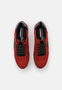 Rote Wildledersneaker mit schwarzen Akzenten, runder Spitze und schwarzen Schnürsenkeln. Sie verfügen über eine Memory Foam-Innensohle und eine gestickte Verzierung entlang der Seiten.