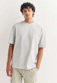 Helehall, lühikeste varrukatega T-särk, valmistatud pehmest puuvillast; omab ümmargust kaelust ja lõdvestunud istuvust, koos kergemate beežide cargo lühikestega.