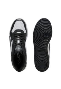 Sneaker Puma bianco e nero mostrato dalla vista superiore e dalla suola, con lacci, punta perforata e un motivo a trazione circolare con il logo Puma.