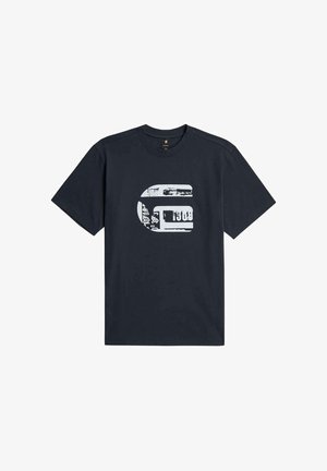 Mann, der ein schlichtes dunkelblaues T-Shirt mit kurzen Ärmeln und ausgewaschene graue Jeans trägt, von hinten vor einem einfarbigen weißen Hintergrund gezeigt.