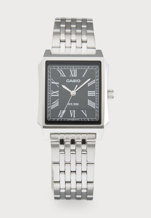 Srebrny zegarek Casio z prostokątną czarną tarczą, srebrnymi rzymskimi cyframi i połączonym metalowym paskiem, pokazujący czas 10:08:36.