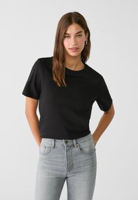 Sort kortærmet T-shirt lavet af glat stof med rund halsudskæring, parret med højtaljede grå jeans med kobbernitter.