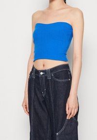 Blå, ribbad, strapless crop top i kombination med mörk denim byxor med vida ben, med vit sömnad och sidofickor.
