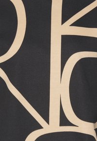 Tessuto nero caratterizzato da grandi lettere e forme beige che creano un design astratto. Il materiale appare morbido e dal tocco strutturato, senza cuciture visibili.