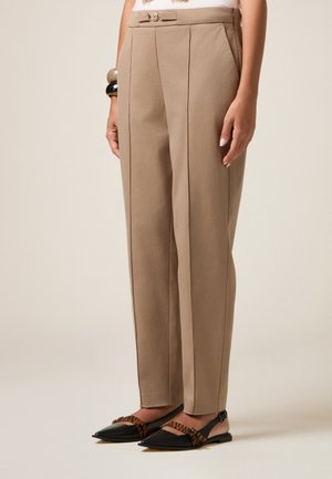 Pantalons beiges taille haute avec deux plis à l'avant, un détail en nœud à la taille, assortis à des ballerines noires à bout pointu avec des accents à motifs.