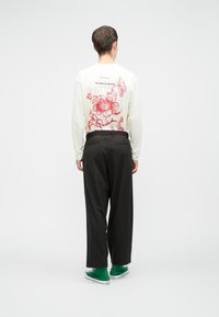 Hosszú ujjú, krémszínű ing piros virágmintával a hátsó részen, laza fekete nadrággal és zöld sportcipővel párosítva.