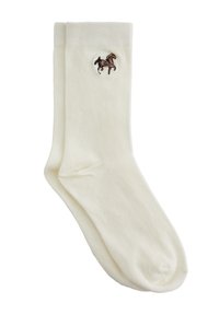 Calcetines de algodón color crema con un pequeño logo de caballo bordado en marrón cerca de la parte superior. Textura suave, forma estándar.
