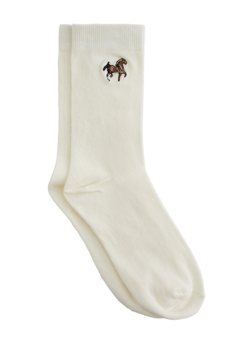 Calcetines de algodón color crema con un pequeño logo de caballo bordado en marrón cerca de la parte superior. Textura suave, forma estándar.