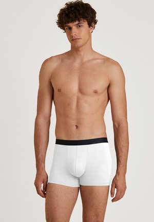 Weiße Boxershorts aus weichem Material mit einem schwarzen elastischen Bund, der den Markennamen trägt. Enganliegendes Design mit Midi-Länge bis zum Oberschenkel.