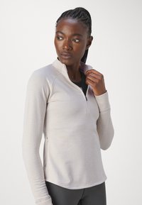 Haut marron clair à fermeture éclair et à manches longues avec un motif texturé. Présente un col haut et une coupe ajustée, fabriqué à partir d'un matériau extensible.