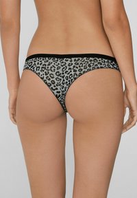 Leopardenmuster-Stringtanga mit einem schwarzen elastischen Bündchen, aus einem durchsichtigen Material gefertigt, mit einer glatten Textur und einem minimalistischen Design.
