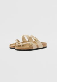 Beige sandaalit, joissa on korkkipohja, kaksi säädettävää hihnaa kullanvärisillä soljilla, kumipohja ja minimalistinen muotoilu.