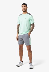 lichtgroen sport t-shirt met grijze schouderaccenten en grijze shorts met een mintgroen paneel. Witte sneakers maken de outfit compleet.