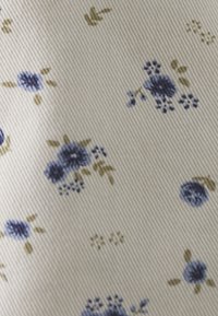 Tissu en coton avec une base crémée texturée présentant un motif floral de fleurs bleues et vertes, certaines avec de petites feuilles, et des détails légers.