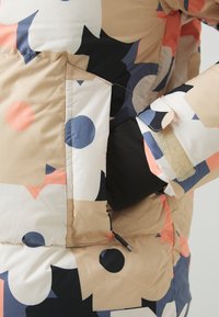 Flerfärgad puffjacka med abstrakta former i beige, marinblå och koralltoner. Inkluderar en ficka med kardborreknäppning. Slät textur.