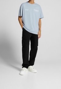 Ljusblå bomulls-t-shirt med vit text, ihop med svarta cargo-byxor med flera fickor och vita sneakers. Enkelt, avslappnat klädesplagg.