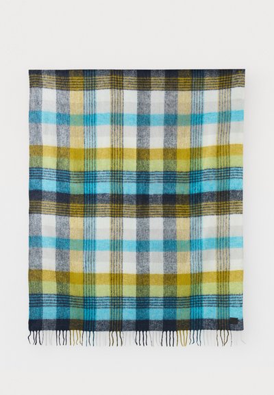 Koc w kratę z mieszanki wełny. Oferuje duże kwadraty w kolorach niebieskim, żółtym, zielonym, szarym i białym. Frędzlowane krawędzie z ciemnym akcentem materiałowym.